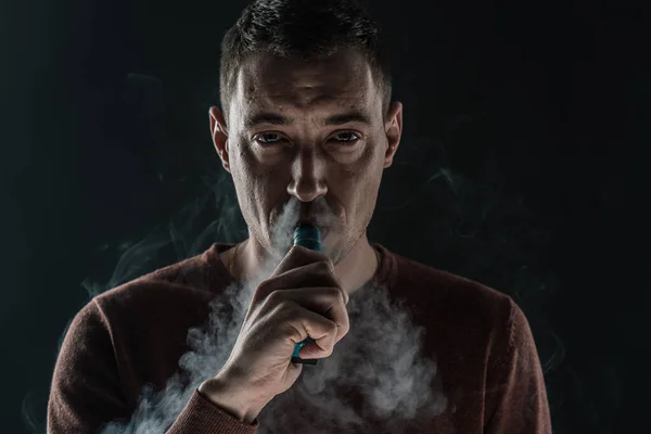 Un homme fume une vape sur un fond noir blanc fumée vapeur portrait gros plan — Photo