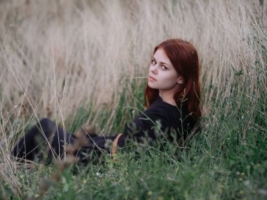 Siyah elbiseli kızıl saçlı kadın doğada kuru çimenlerin üzerinde yatıyor.