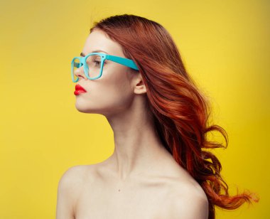 Çıplak omuzlu bir kadın. Mavi gözlükler. Kırpılmış saçlar.