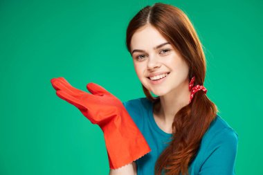 Kırmızı lastik eldivenli neşeli güzel kadın, yeşil arka planı temizliyor.