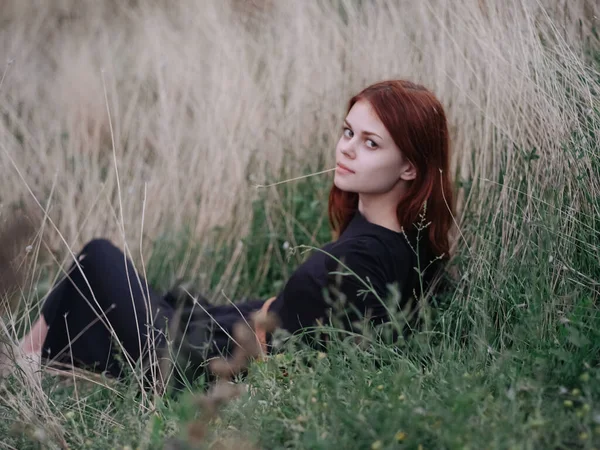 Rothaarige Frau in schwarzem Kleid liegt auf trockenem Gras in der Natur — Stockfoto