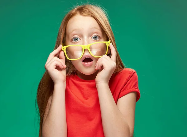 Chica con el pelo rojo usando gafas amarillas posando emociones recortado ver estudio escuela —  Fotos de Stock