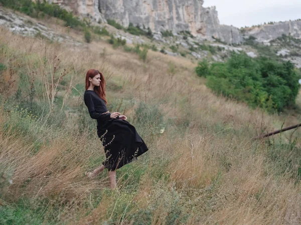 Mulher de vestido preto na floresta nas montanhas na grama seca no prado — Fotografia de Stock