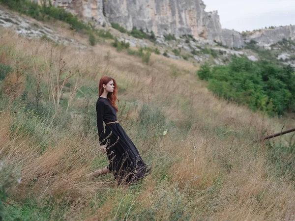 Mulher de vestido preto na floresta nas montanhas na grama seca no prado — Fotografia de Stock