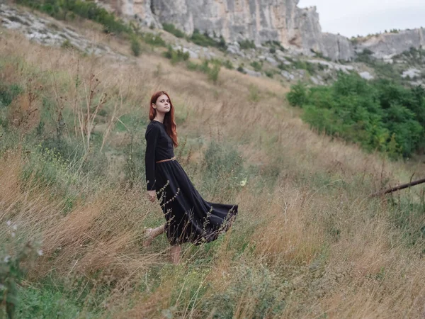 Mulher de vestido preto ao ar livre nas montanhas em um prado no outono — Fotografia de Stock