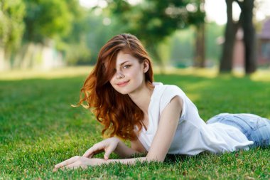Sevimli kızıl saçlı kadın parkın bahçesindeki çimlerde yatıyor.