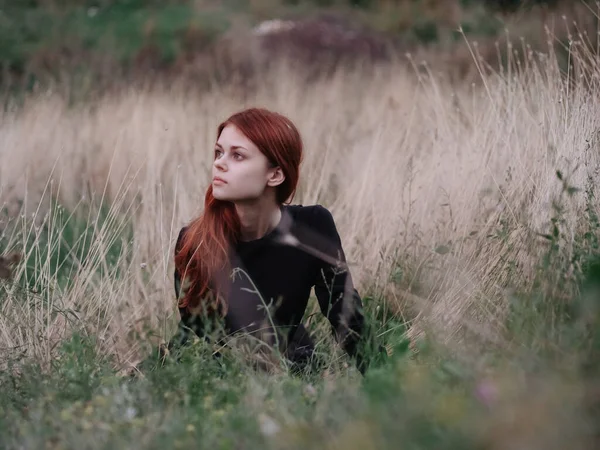 Femme aux cheveux roux dans une robe noire se trouve dans la forêt sur l'herbe sèche dans la nature — Photo