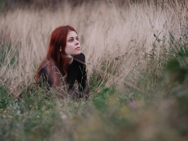 Vörös hajú nő fekete ruhában fekszik egy mezőn száraz fű a természetben — Stock Fotó