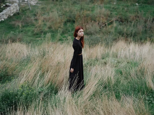 你是一个穿着黑色衣服的女人，在山中的草地上，走在干草上，走向大自然 — 图库照片