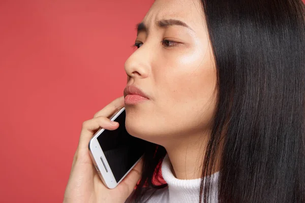Женщина азиатской внешности разговаривает по телефону эмоции неудовлетворенности крупным планом красный фон — стоковое фото