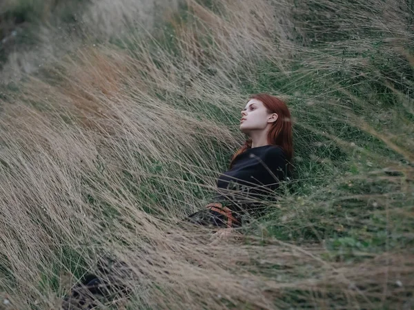Une femme en robe noire repose sur l'herbe sèche dans une prairie dans les montagnes — Photo