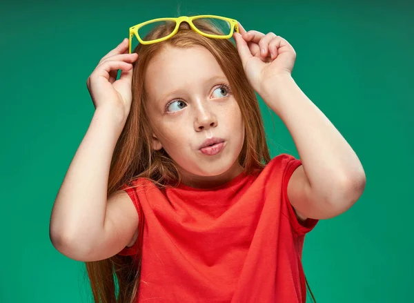 Mignonne fille aux cheveux roux avec des lunettes gestuelle avec ses mains école fond vert — Photo