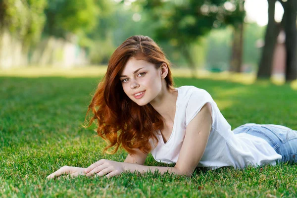 Руда жінка лежить в парку на газоні на свіжому повітрі — стокове фото