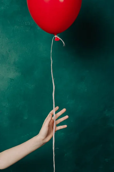 Globo rojo inflable en una mano femenina sobre un fondo verde de cerca —  Fotos de Stock