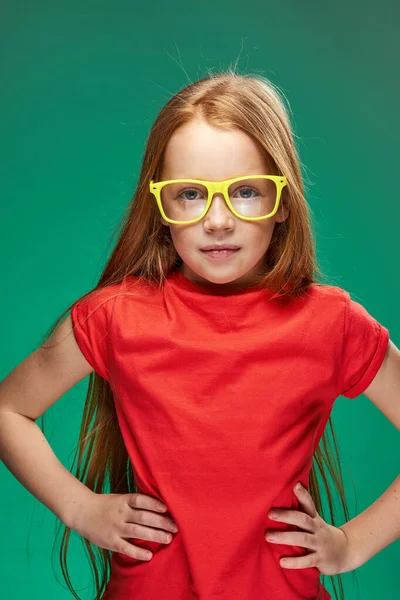 Συναισθηματική κοκκινομάλλα κορίτσι σε κίτρινα γυαλιά κόκκινο t-shirt συναισθήματα στούντιο πράσινο φόντο — Φωτογραφία Αρχείου