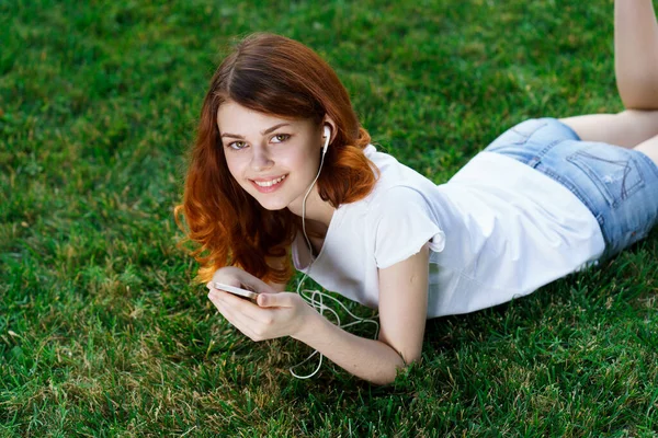 Frau liegt mit Handy in der Hand auf dem Rasen und entspannt im Park — Stockfoto
