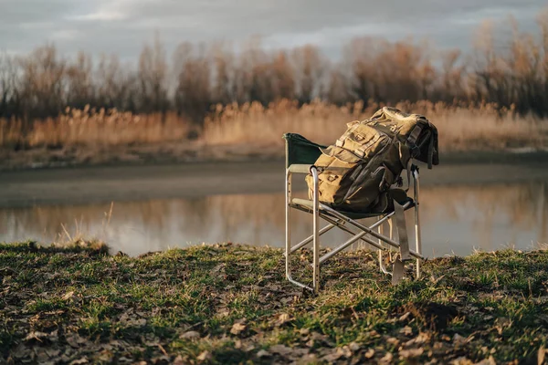 Katlanan sandalyede büyük bir turist çantası balık avlama gölü doğası — Stok fotoğraf