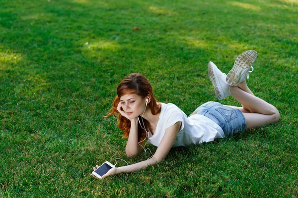 Vacker kvinna ligger på gräsmattan utomhus i parken vila telefon i händerna — Stockfoto