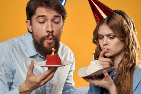 노란색 배경에 손에 케이크를 들고 모자를 쓴 생일 파티를 하는 남자와 여자 — 스톡 사진
