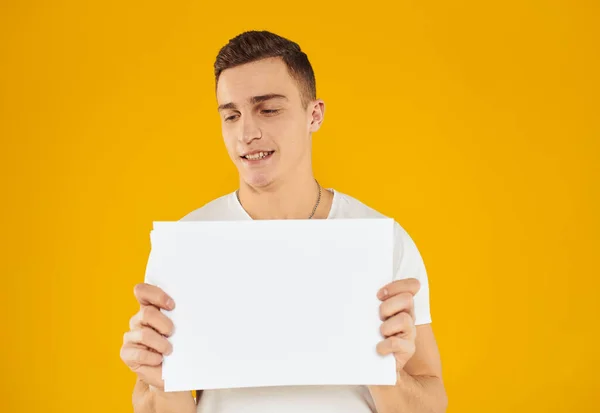 Ein Mann in einem weißen T-Shirt mit einem Blatt Papier auf gelbem Hintergrund. — Stockfoto