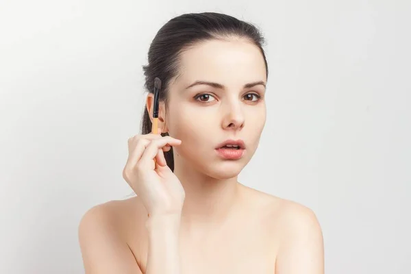 Attraktive Brünette mit Creme auf dem Gesicht Pinsel in den Händen Make-up — Stockfoto