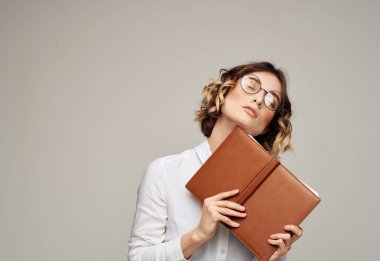 İş kadını, elinde açık bir defter, yüzünde gözlük, beyaz gömlekli.