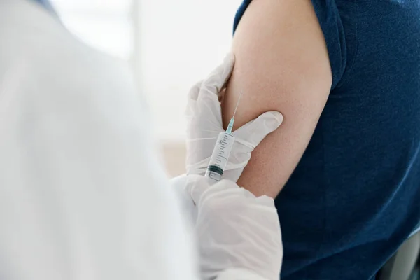 Doctora en una máscara médica inyectando a un hombre en una camiseta azul covid — Foto de Stock