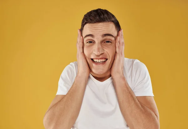 An energetic guy in a white T-shirt touches his head with his hand on a yellow background — Stock Photo, Image