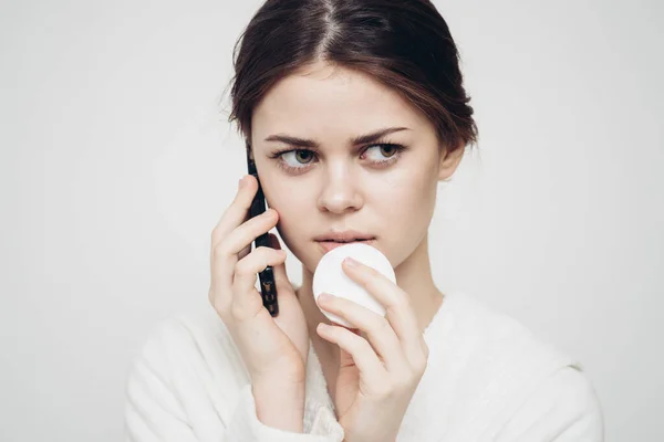 Mujer con un teléfono móvil sostiene una esponja en su mano sobre un fondo claro — Foto de Stock