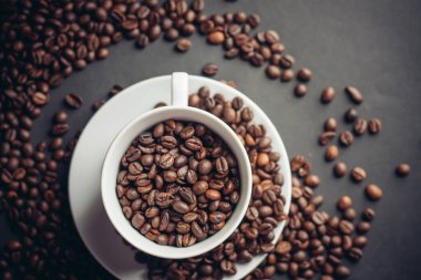 Kahve çekirdekleri bir fincanda ve beyaz fincan altlıkları yakın plan gri.