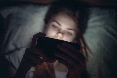 Geceleri elinde telefon olan gülümseyen bir kadın yatakta yaşam tarzı iletişiminde yatıyor.