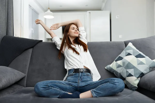 Mujer alegre sosteniendo sus manos detrás de su cabeza relajándose en el sofá en el apartamento — Foto de Stock