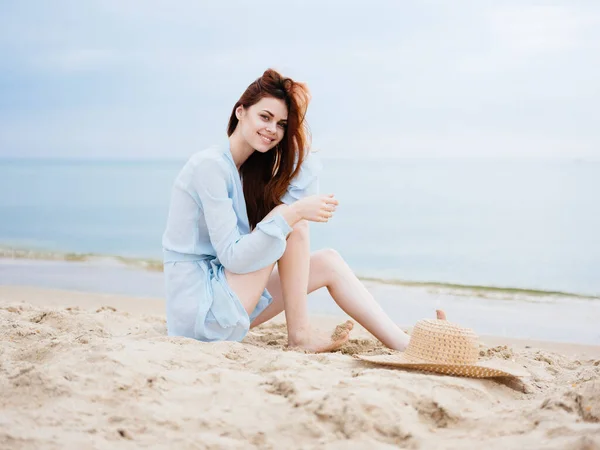 Una donna romantica in un abito blu trasparente siede sulla sabbia vicino al mare e sorride — Foto Stock