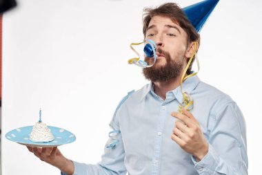 Sakallı bir adam arka planda hafif bir doğum gününde elinde pasta tutuyor.