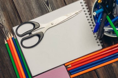 Tahta bir masanın üzerindeki kırtasiye kağıdı açık not defteri makasları renkli kalemler notu