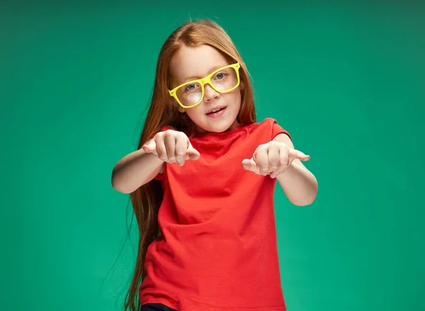 Aranyos vörös hajú lány gesztikulál kezével gyermekkori zöld háttér iskola — Stock Fotó