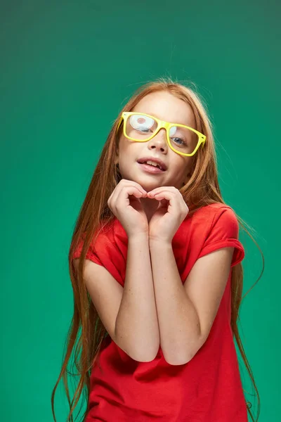 Χαριτωμένο κορίτσι με κόκκινα μαλλιά με γυαλιά gesturing με τα χέρια της σχολείο παιδική ηλικία πράσινο φόντο — Φωτογραφία Αρχείου