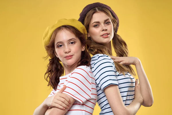 Χαρούμενες αδελφές με καπέλα ριγέ T-shirts χαρά τρόπο ζωής κίτρινο φόντο οικογένεια — Φωτογραφία Αρχείου