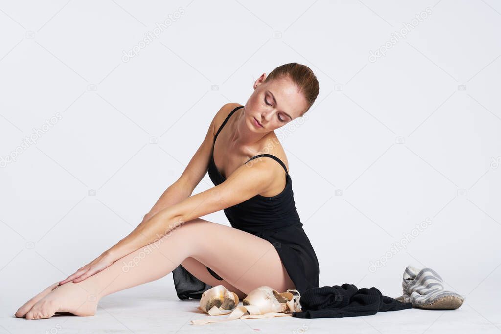 A ballerina in a black dress on a light background performs dance exercises striped socks planty tutu model
