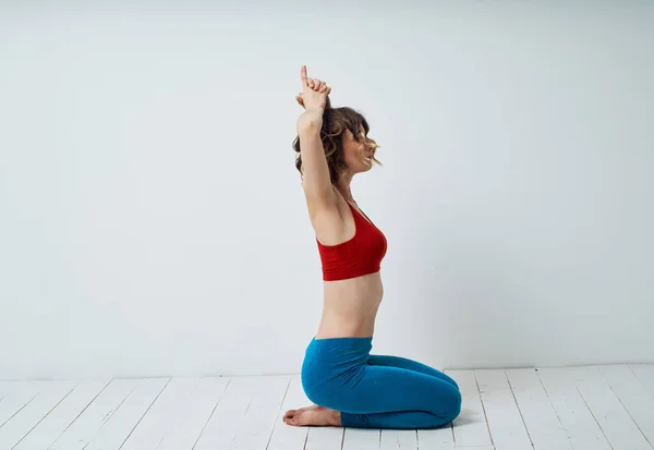 Štíhlá žena ukazuje cvičení na jógu ve světlé místnosti, sedící na podlaze s rukama nad hlavou — Stock fotografie