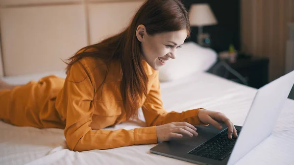 Kadın dizüstü bilgisayarın önünde yatağa uzanıyor. Serbest iş interneti. — Stok fotoğraf