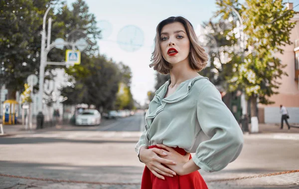 Una mujer en una falda de camisa pasea por las calles centrales de la ciudad y edificios altos en el fondo —  Fotos de Stock