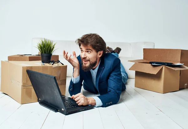 Un homme en costume repose sur le sol avec des boîtes de bureau déballer une technologie d'ordinateur portable — Photo