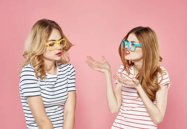 Két vidám barátnő csíkos pólóban egymás mellett állnak rózsaszín háttéren. — Stock Fotó