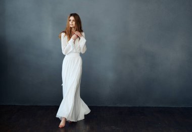 Beyaz elbiseli, kızıl saçlı bir kadın. Gri bir arka planda.