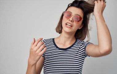 Gözlüklü ve çizgili tişörtlü güzel bir kadın. Kırmızı etek, gri arka plan.