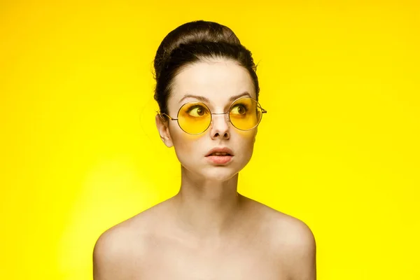 Kadının çıplak omuzları şaşkın, sarı gözlüklü, izole bir arka plan. — Stok fotoğraf