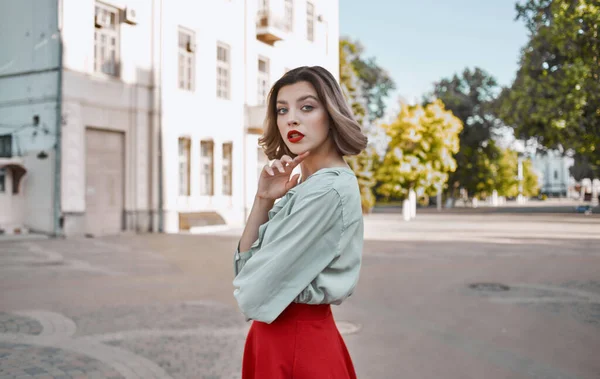 Женщина с ярким макияжем в рубашке и в красной юбке ходят по улице летом возле здания — стоковое фото