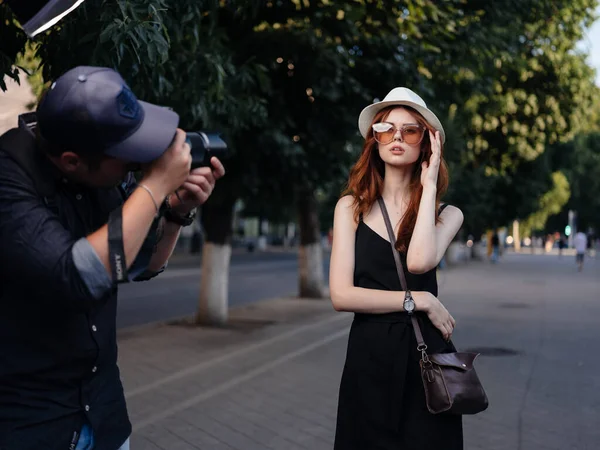 Modna kobieta w czarnej sukience i w białym kapeluszu spoczywają w naturze na ulicy w parku — Zdjęcie stockowe