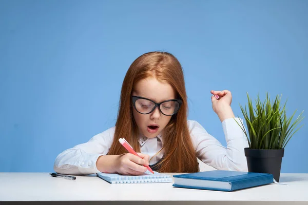 テーブルスクールで宿題をしている眼鏡をかけた赤い髪の少女 — ストック写真